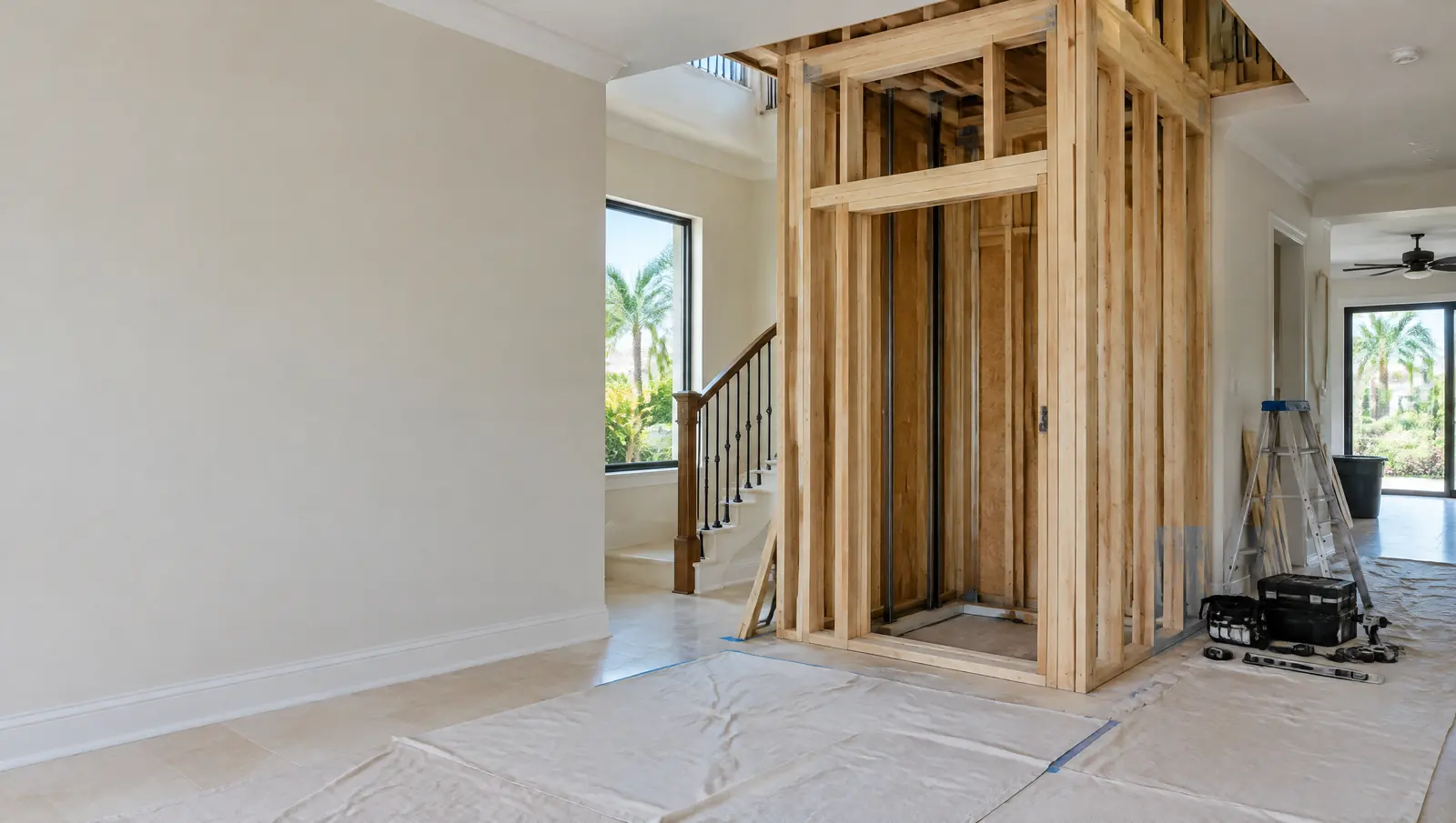 New timber-framed elevator shaft inside an existing Florida home during a retrofit, with dust sheets on the floor
