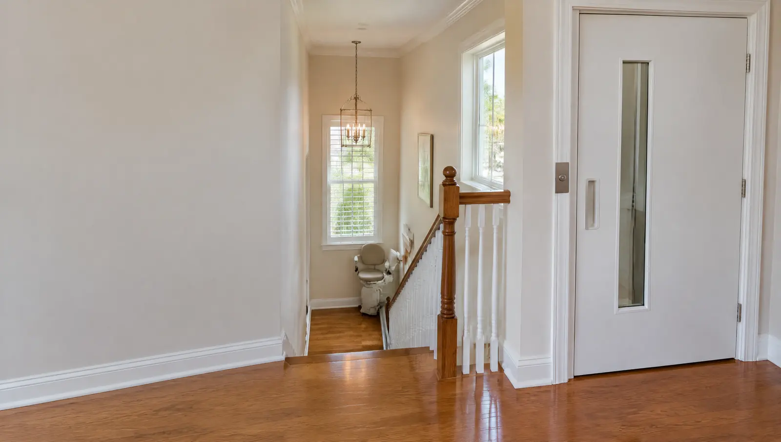 View from an upstairs landing past an elevator hall door down to a stair lift parked at the foot of the stairs
