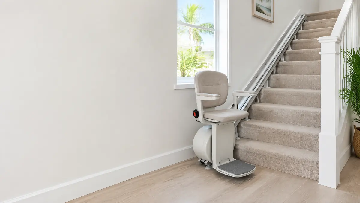 Straight stair lift with a cushioned seat at the bottom of a carpeted staircase in a bright home