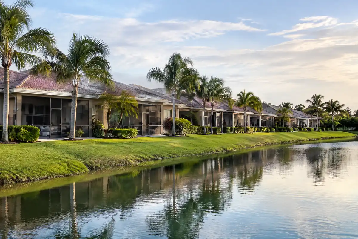 Single-storey attached villa homes with screened lanais beside a lake in a Palm Beach County community