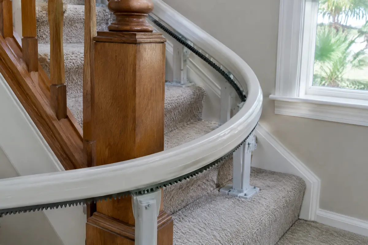 Curved stair lift rail bending around the turn of a staircase beside a wooden newel post