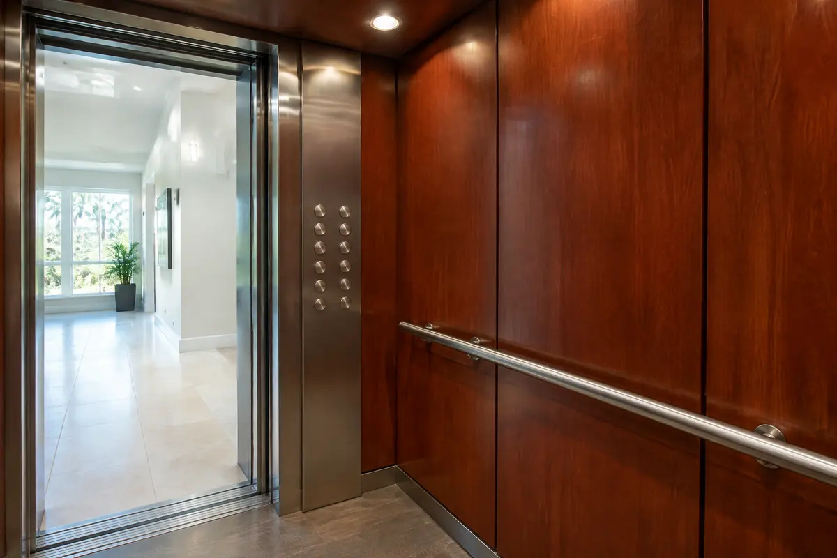 Inside a home elevator cab with wood panels, a handrail, soft ceiling lights and a plain button panel