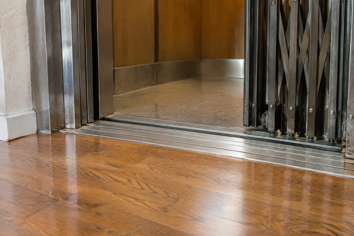 Close view of a home elevator landing sill and the edge of the cab gate, showing the small gap between them