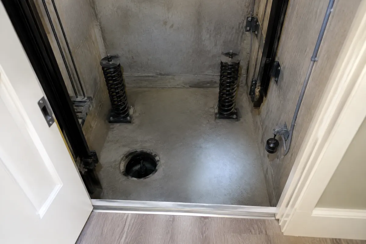 Looking down into a clean, dry home elevator pit with buffer springs and a float switch on the pit wall
