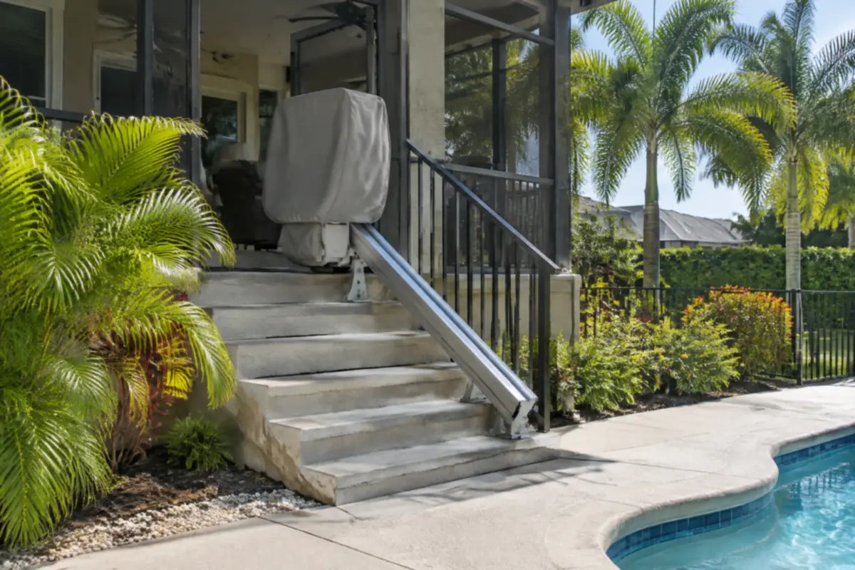 Outdoor stair lift with a weather cover on steps from a raised lanai down to a pool deck