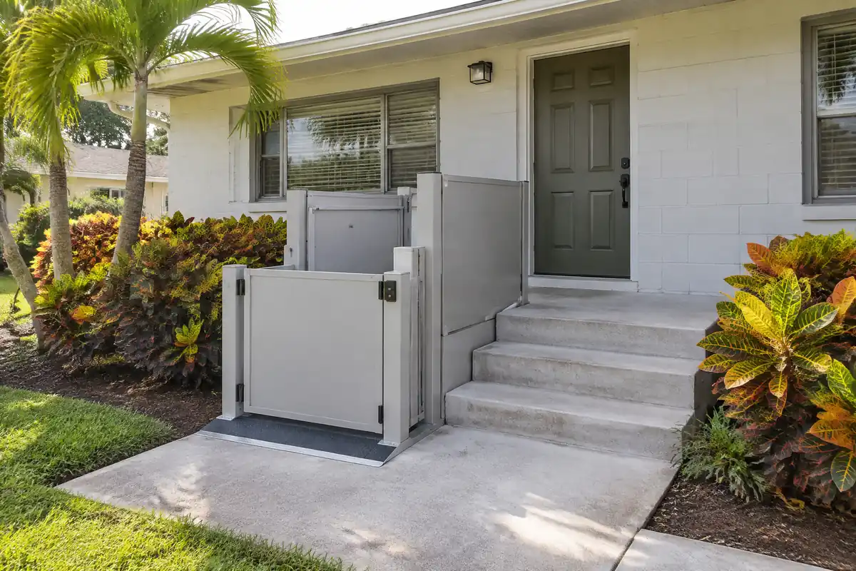 Compact open porch lift with a gate beside three concrete steps to the door of a single-storey home